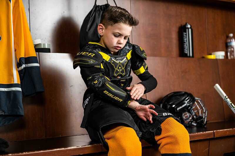 Malý kluk si obléká hokejovou výstroj Bauer